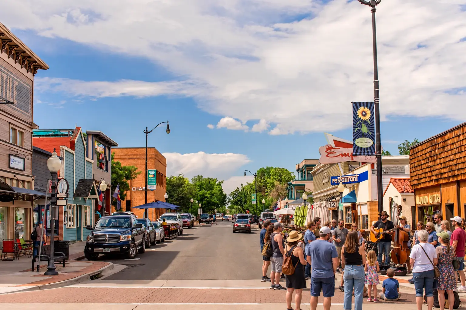 A crowd gathered on the brick sidewalk of downtown Louisville, Colorado, listening to a guitarist and upright bass player on a sunny afternoon